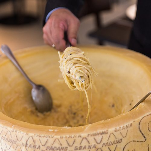 Chef making spaghetti carbonara in cheese wheel with tourched brandy and fried bacon.